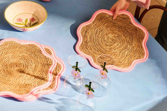 Woven placemats and glasses on a blue tablecloth with a bowl.