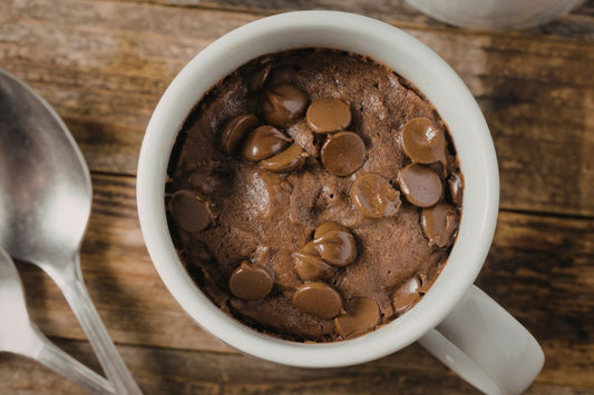 A ceramic mug filled with chocolate cake with chocolate chips toppings on a wooden surface.