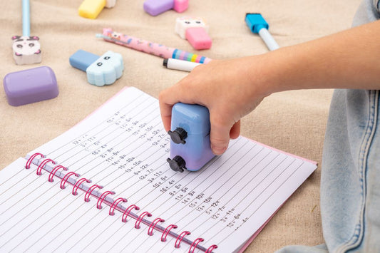 Child's hand using a stamp on a notebook with colorful stationery nearby.