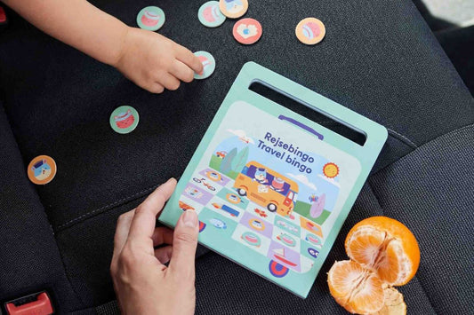 Child's hand playing with tokens beside a book and orange slices.