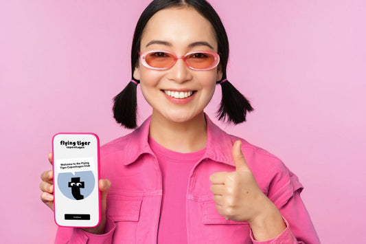 Woman in pink attire showing flying tiger copenhagen app and giving thumbs up.