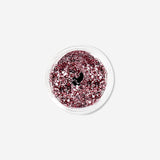 Pink glitter eyeshadow flakes from Flying Tiger Copenhagen, close-up of shimmering, sparkly cosmetic flakes in a jar.