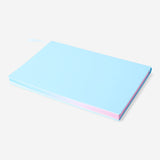 A5 office notebook with rainbow-colored edges by Flying Tiger Copenhagen, open to blank lined pages on a wooden desk.