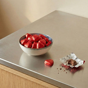 Bowl filled with red foil-wrapped heart chocolates on a metal countertop