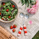 Two stainless steel salad servers with strawberry-shaped handles, designed for serving salads in a stylish kitchen setting.