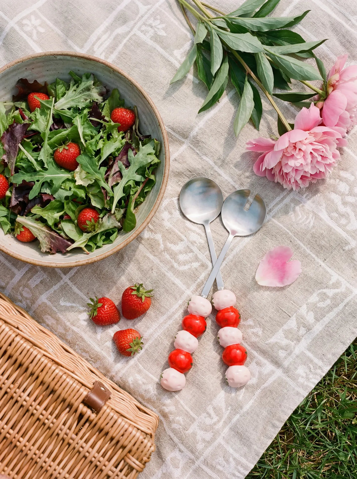 Two stainless steel salad servers with strawberry-shaped handles, designed for serving salads in a stylish kitchen setting.