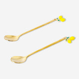 Two gold dessert spoons with lemon-shaped handles from Flying Tiger Copenhagen, shown on a kitchen table.