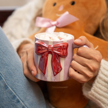 Woman holding a festive mug of hot chocolate with marshmallows beside a gingerbread plush.