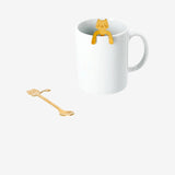 Two gold cat-shaped spoon decorations for hanging on mugs, designed for kitchen use by Flying Tiger Copenhagen.