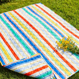 Quilted striped picnic blanket from Flying Tiger Copenhagen, 170x130 cm, showing vibrant striped pattern and soft quilted texture.