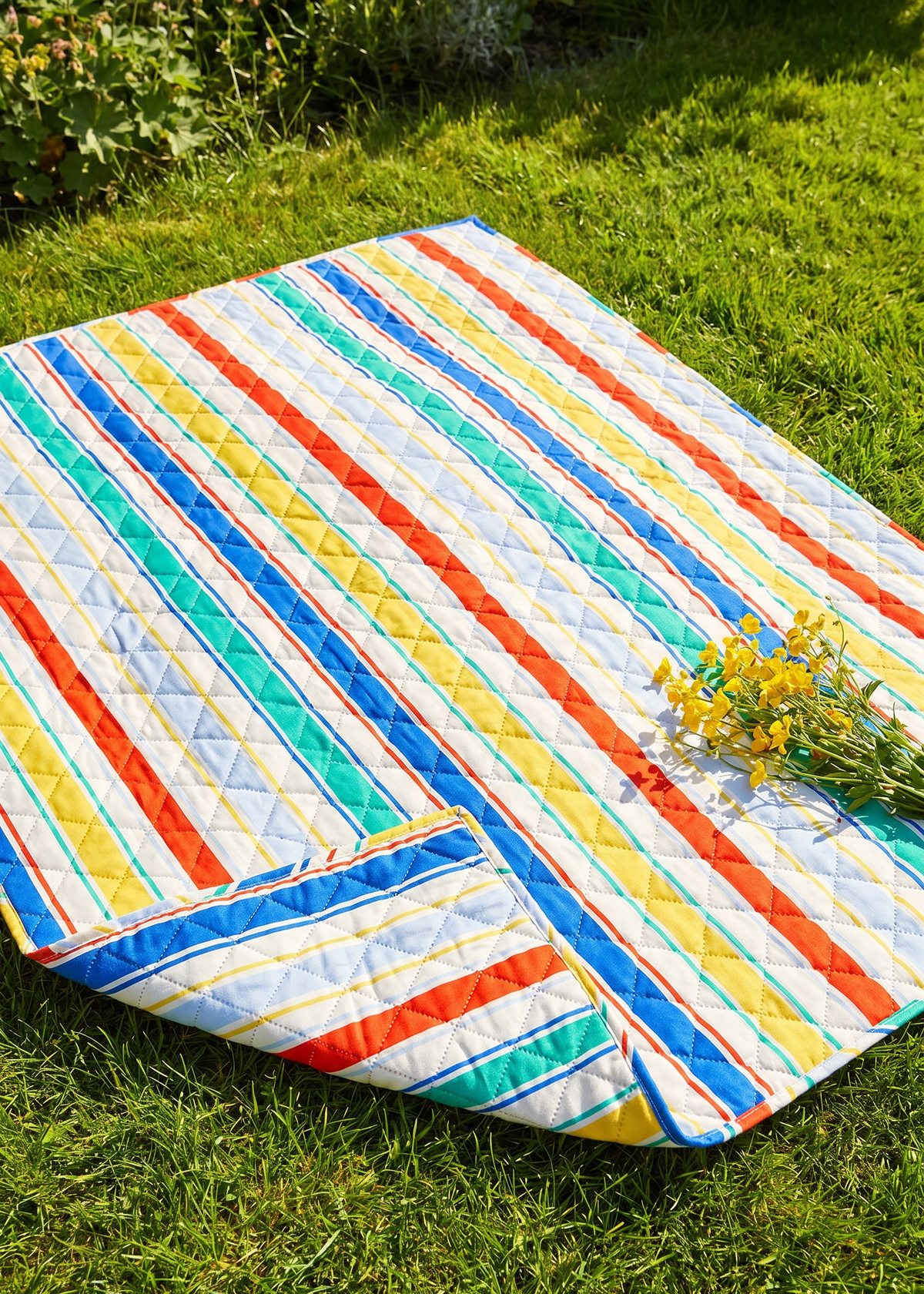 Quilted striped picnic blanket from Flying Tiger Copenhagen, 170x130 cm, showing vibrant striped pattern and soft quilted texture.