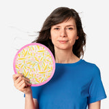 Foldable textile fan with colorful flower print from Flying Tiger Copenhagen, open showcasing its vibrant design and lightweight structure.