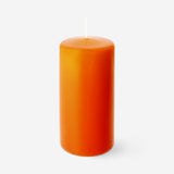 Orange pillar candle from Flying Tiger Copenhagen, 14 cm tall, sitting on a wooden surface with a flickering flame.