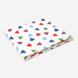 Heart-patterned tablecloth from Flying Tiger Copenhagen, 140x220 cm, showing a cozy home dining setup with colorful heart designs.